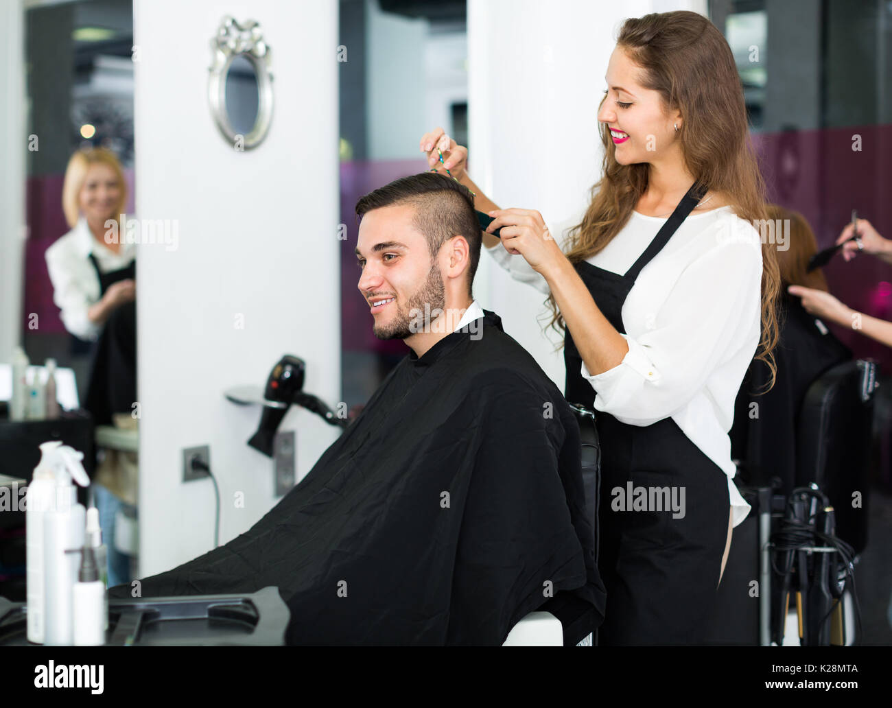 Smiling Female Hairdresser Doing Hairstyle For Young Men At Salon