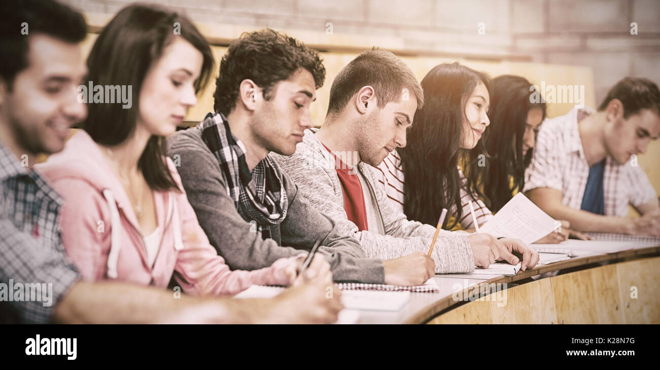 Students writing notes while sitting in row at lecture hall Stock Photo