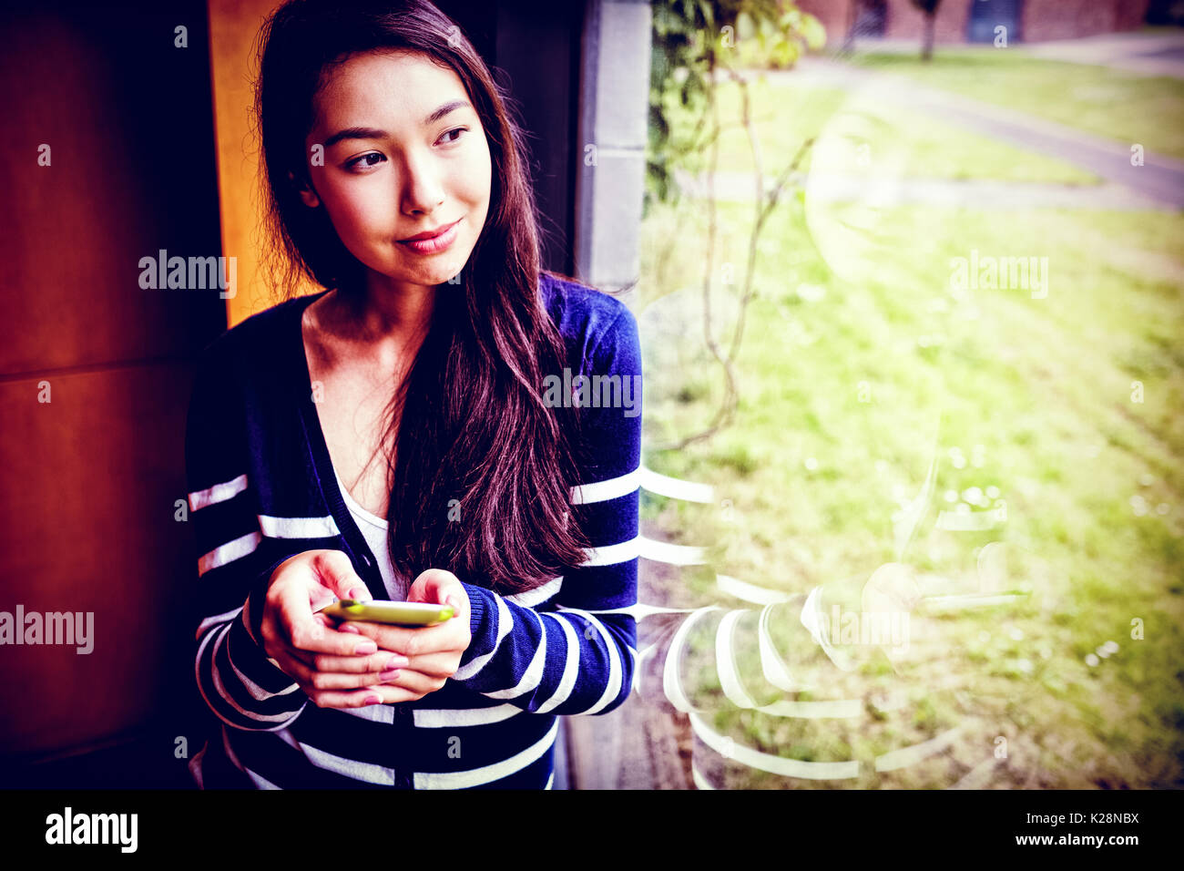Smiling student with smartphone looking through window Stock Photo