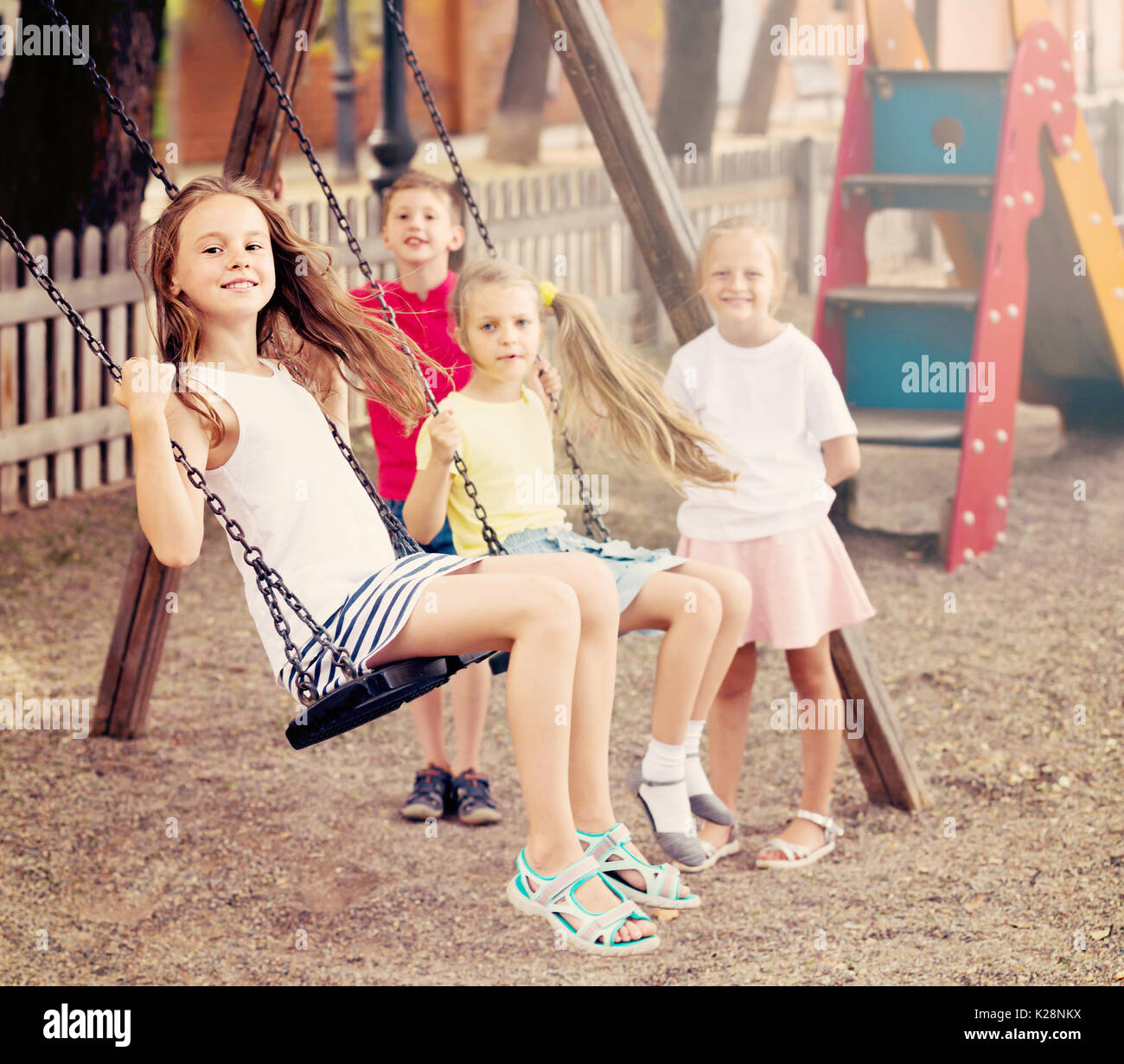 Laughing girls and boys in school age swinging on children's playground outdoors Stock Photo