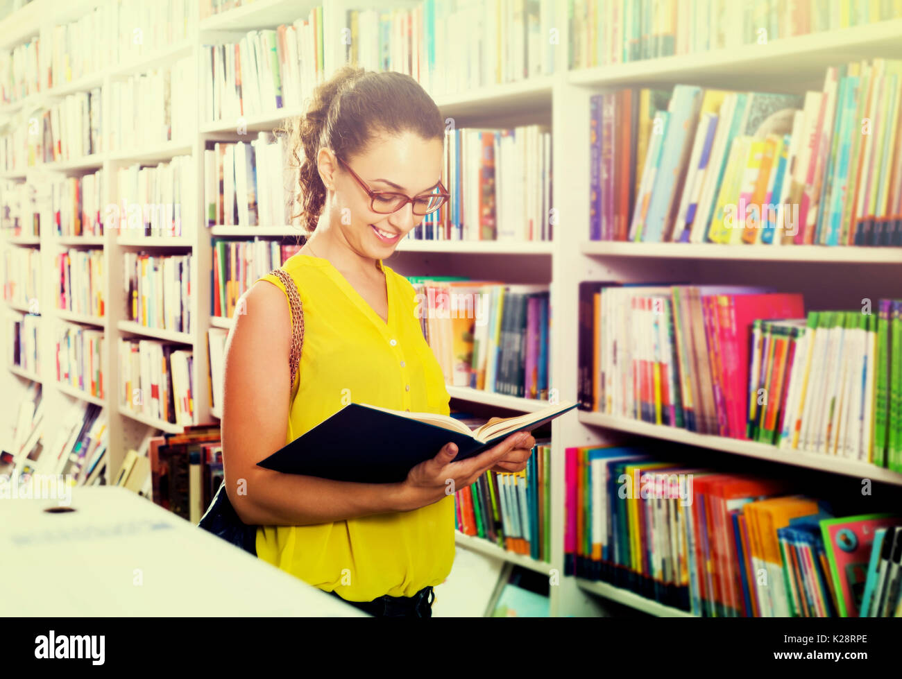 Portrait of smiling young woman looking interested and reading textbook ...
