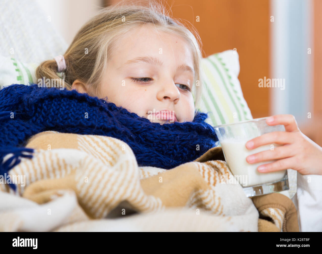 Little girl under blanket with warm milk and fever indoors Stock Photo