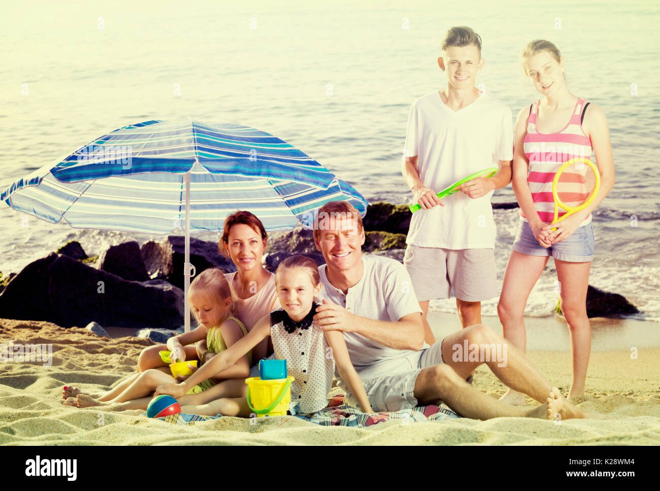 Active family with kids together on beach sitting under umbrella and