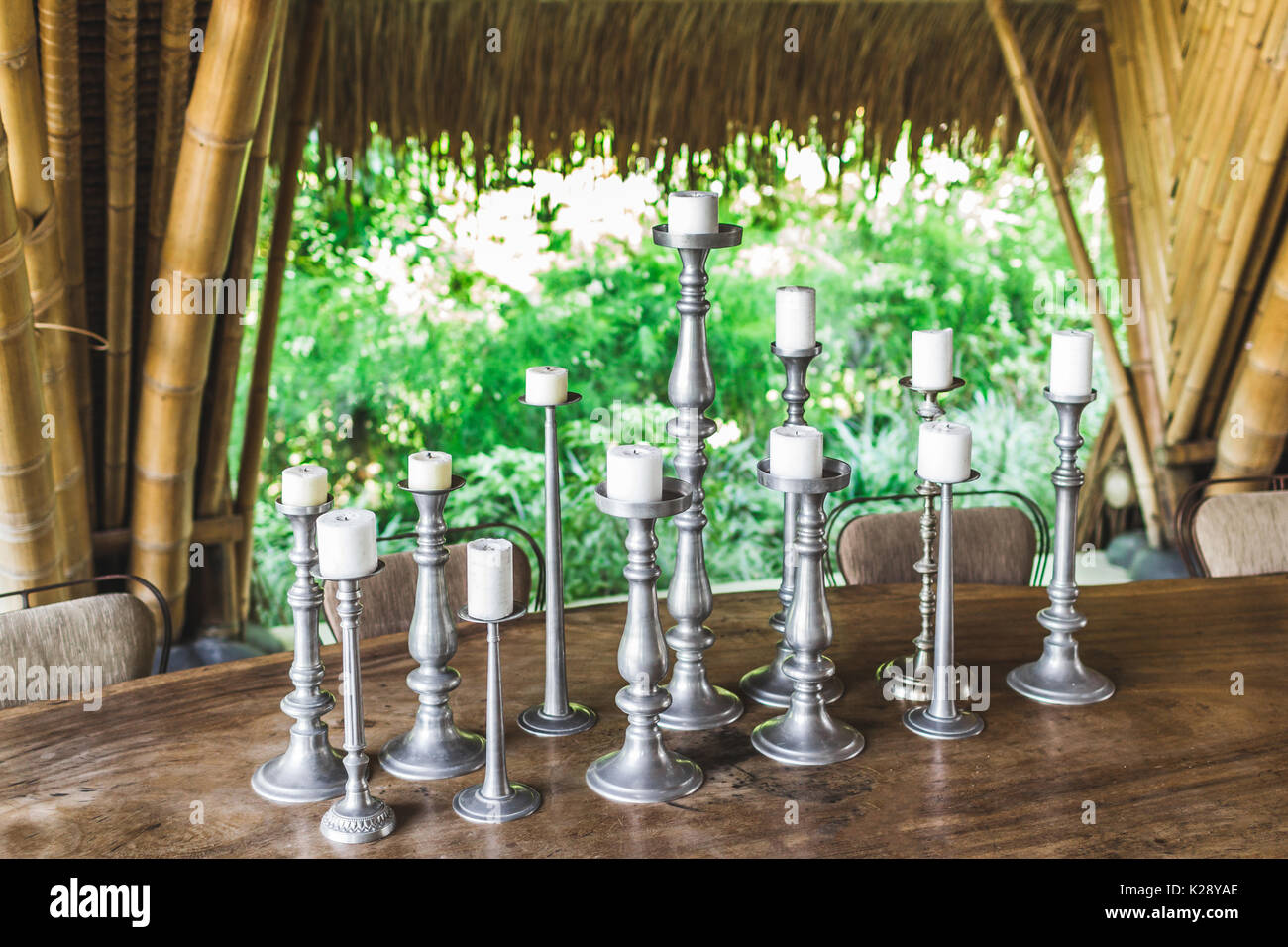 Many white candles in vintage metal candlesticks on wooden table as decoration of restaurant outdoor in garden Stock Photo