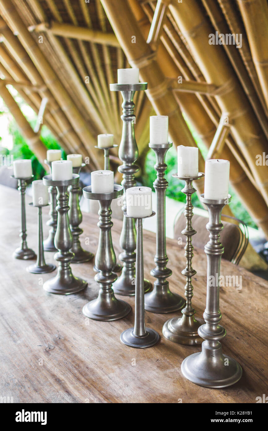 Many white candles in vintage metal candlesticks on wooden table as decoration of restaurant outdoor in garden Stock Photo