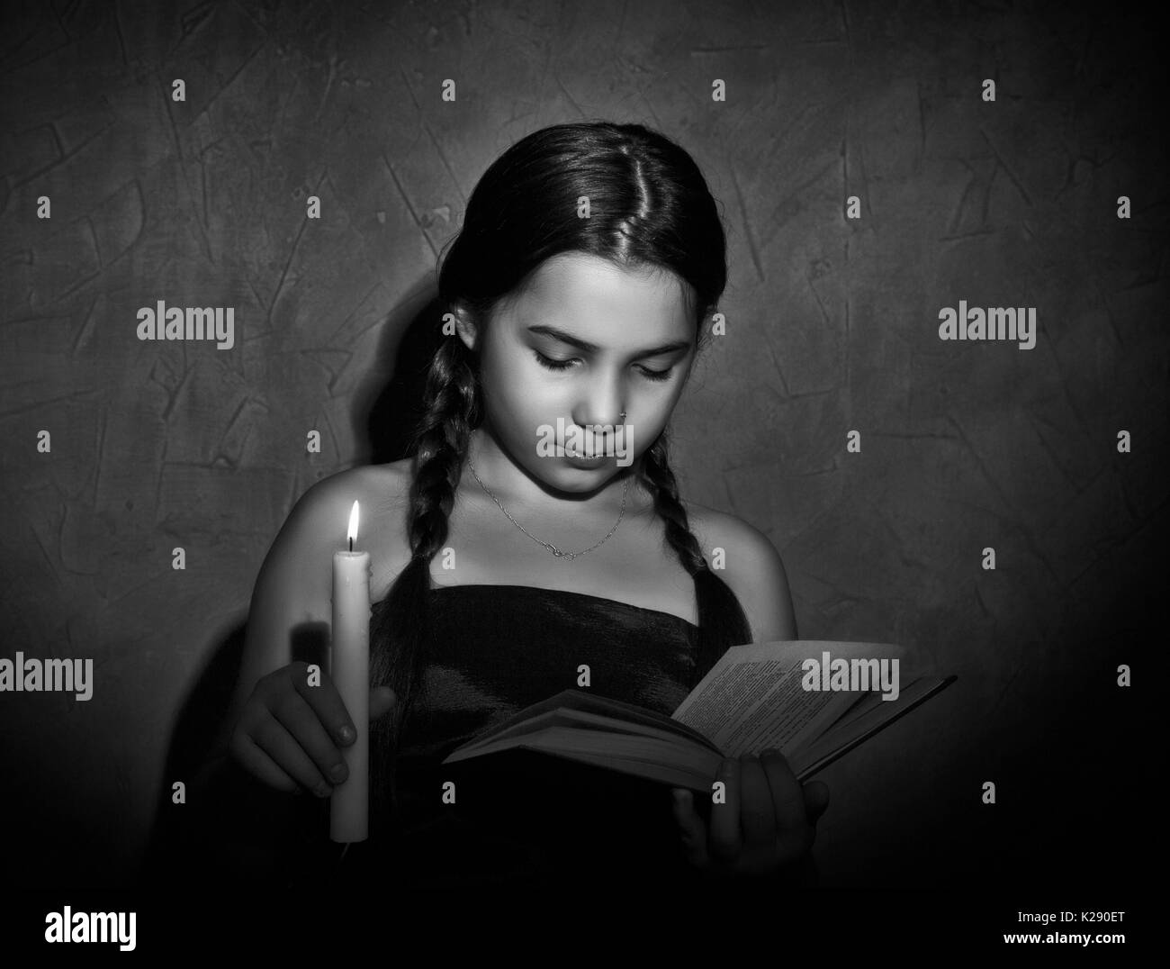 little girl reading book and studying in candle light in dark room