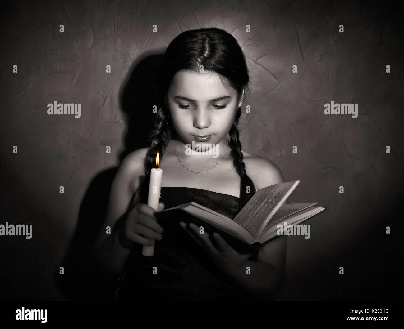 little girl reading book and studying in candle light in dark room