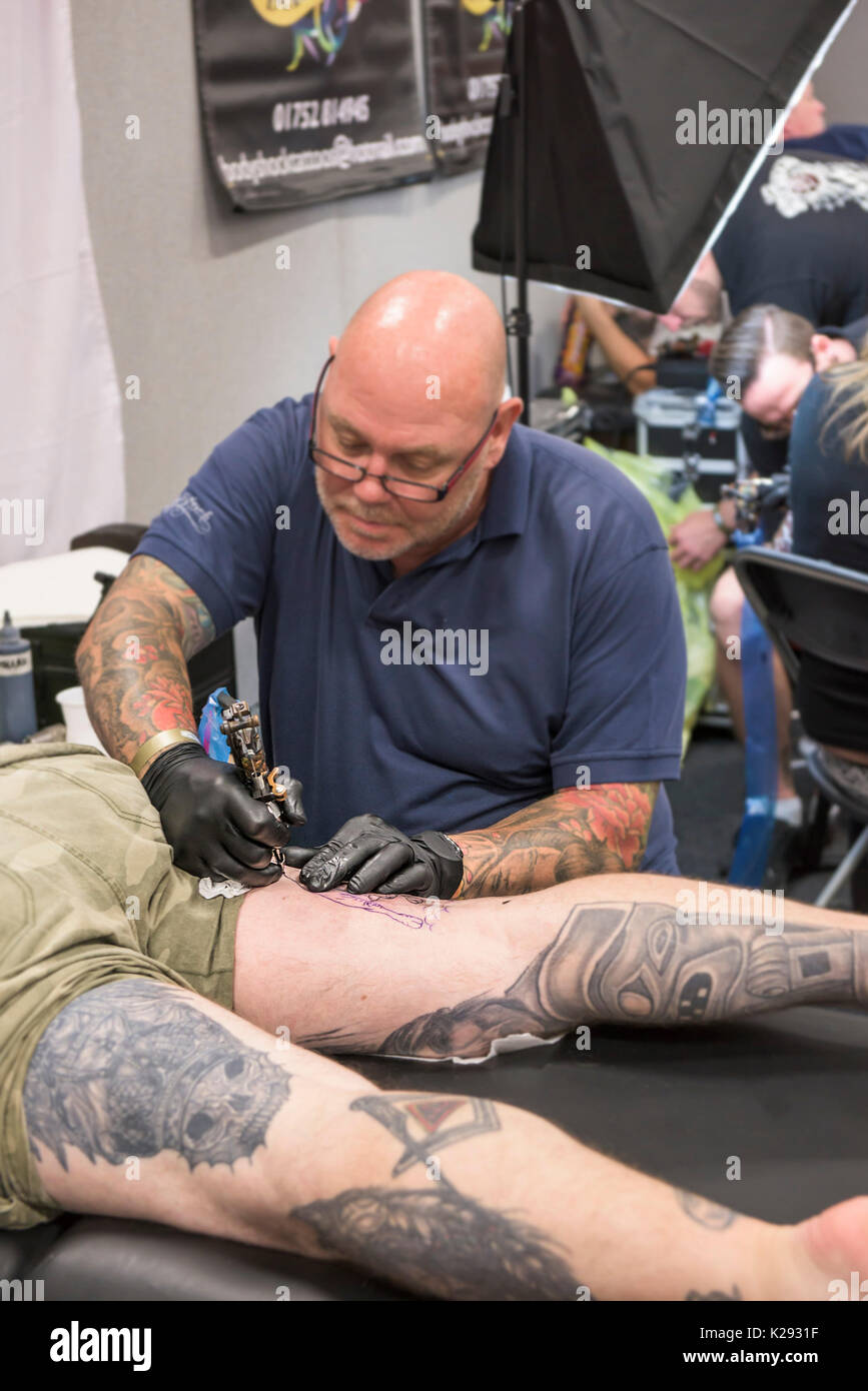 Cornwall Tattoo Convention - a man having his upper thigh tattooed at the Cornwall Tattoo Convention. Stock Photo