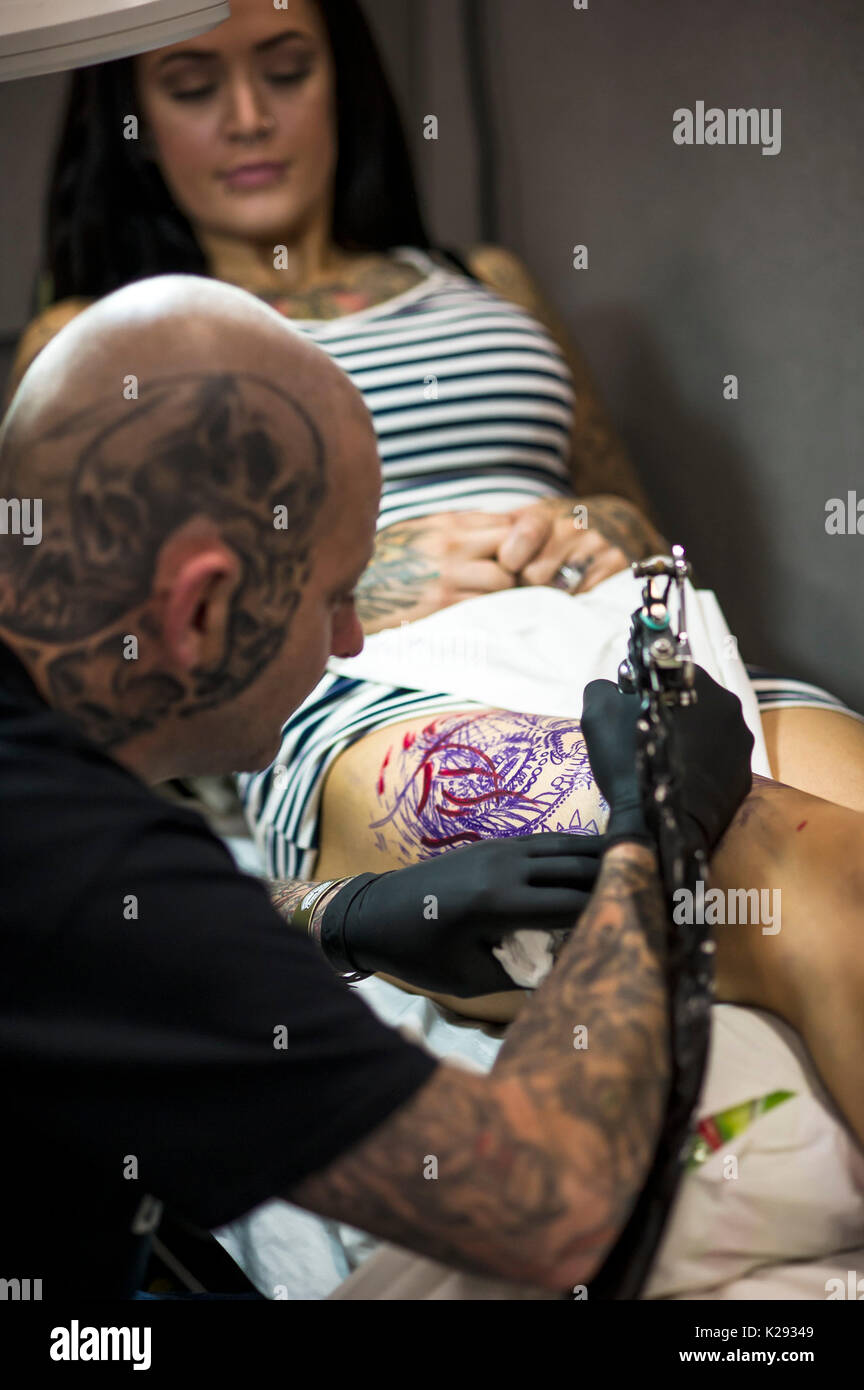 Cornwall Tattoo Convention - a tattooist working on a design on the thigh of a customer at the Cornwall Tattoo Convention. Stock Photo