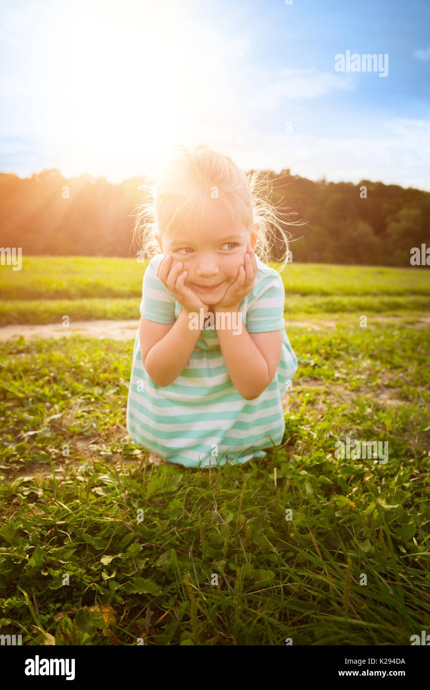 Adorable blond little girl with cheeky smile, outdoors play time Stock Photo