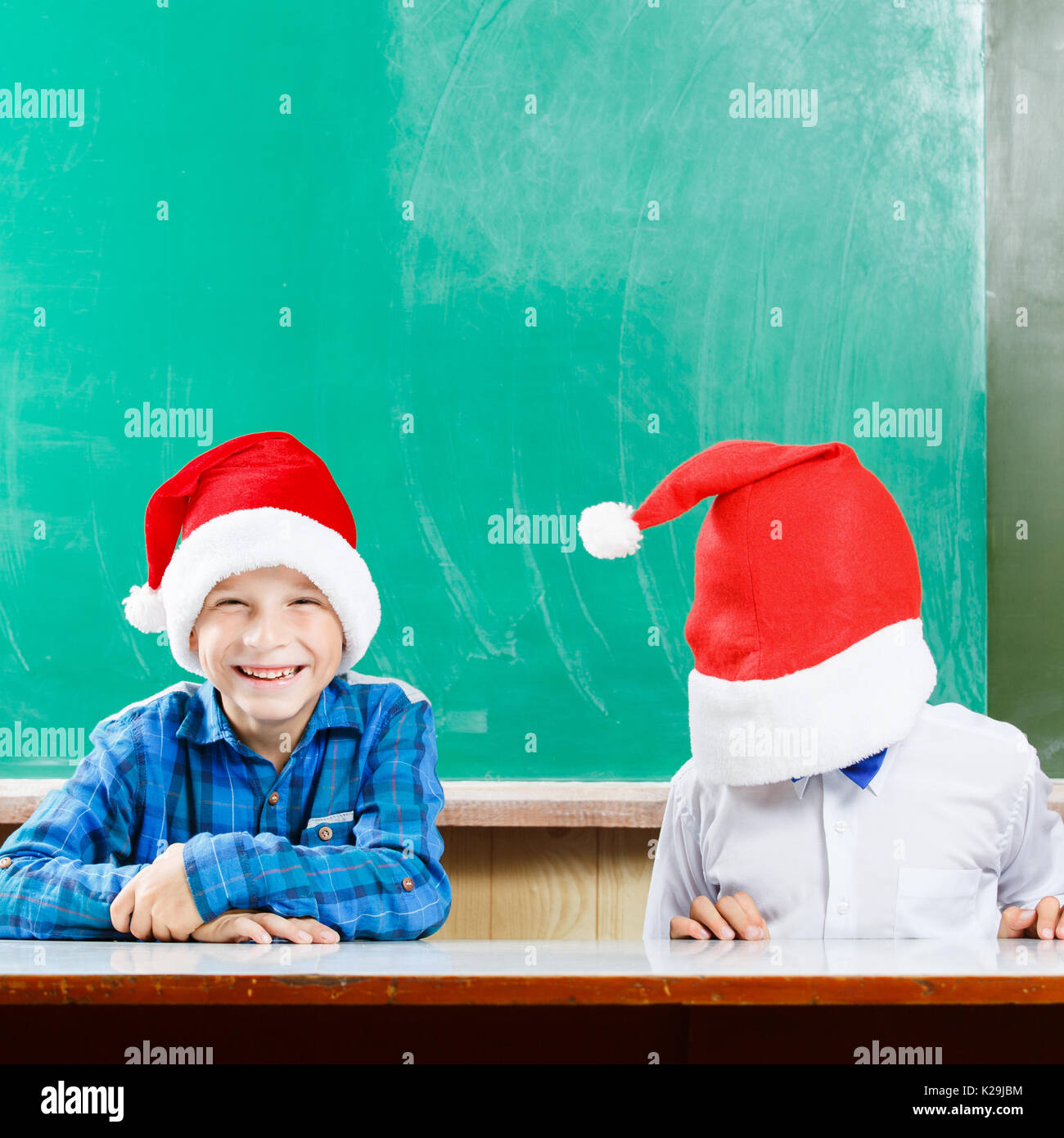 Two boys in santa hats have fun against school blackboard. Christmas concept background with copy space Stock Photo