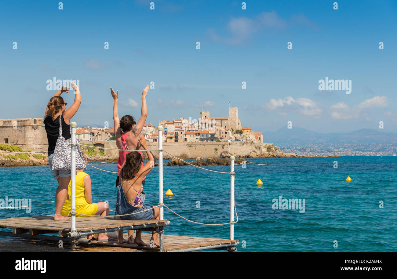 Young women happily wave into the distance with Antibes, France old town in the background Stock Photo