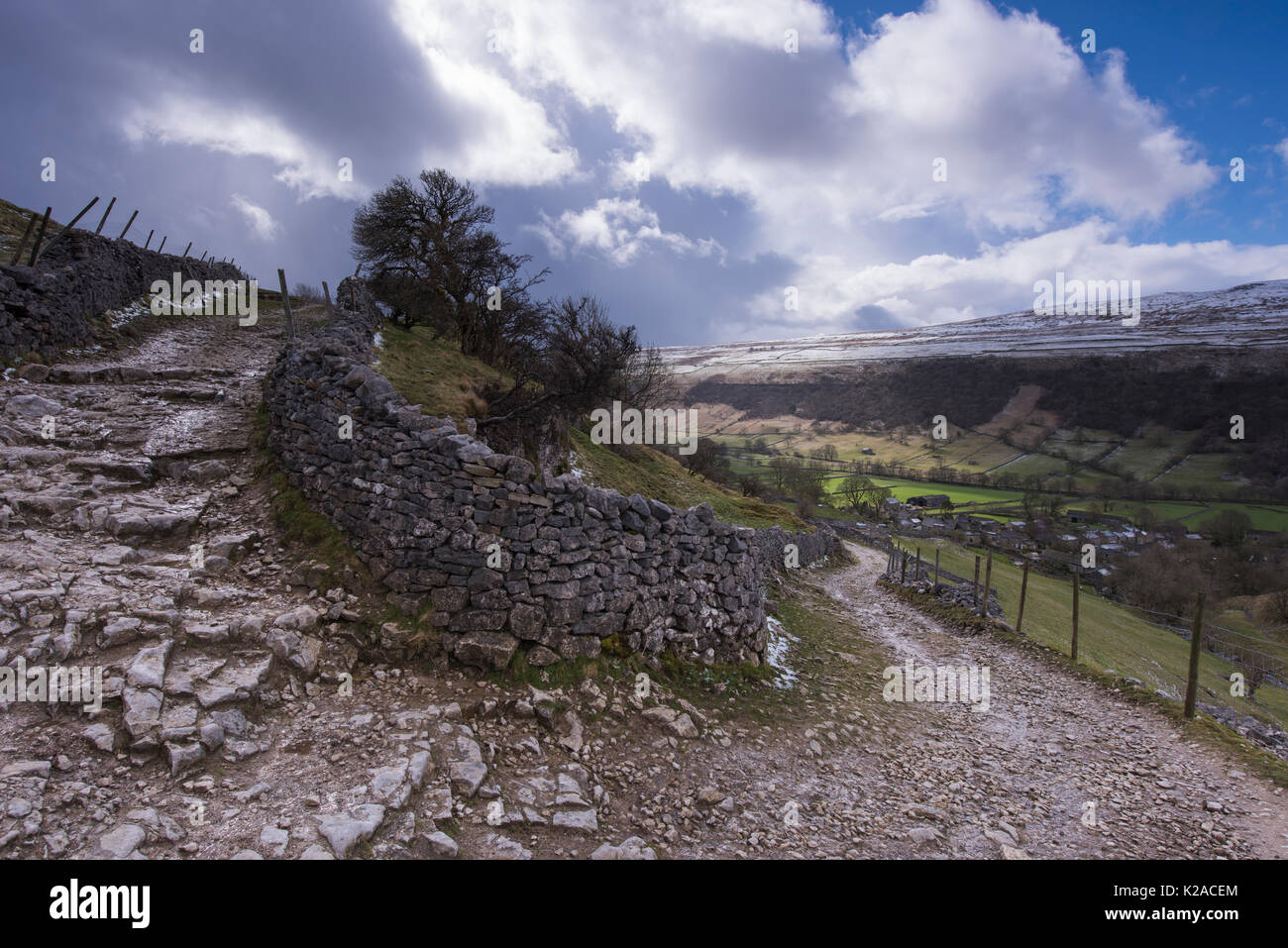 Under blue sky, footpath or stone track, climbs & curves round dry-stone wall, up from Starbotton village, Wharfedale, Yorkshire Dales, England, UK. Stock Photo