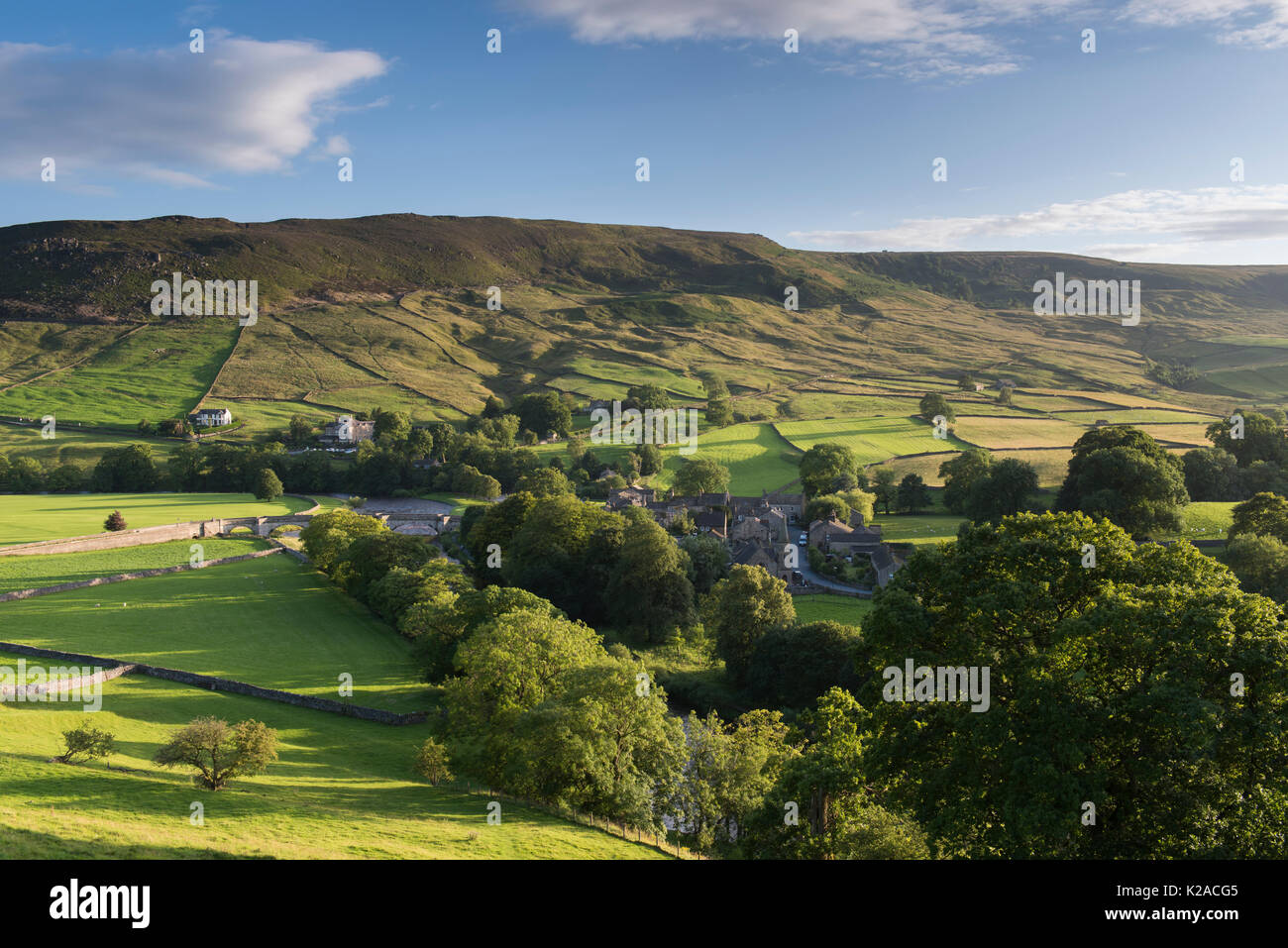 Scenic sunny Burnsall village in River Wharfe valley (hillside slopes, high hills, green fields, pastures, blue sky) - Yorkshire Dales, England, UK. Stock Photo