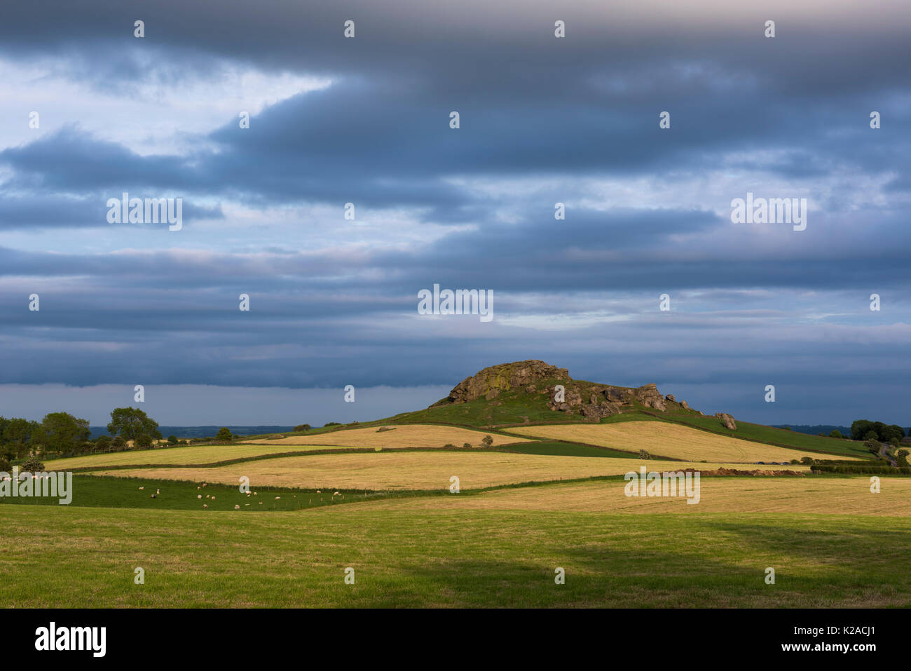 Almscliffe Crag hill lit by sun (gritstone tor, multi-coloured fields, stone walls, beautiful hilly scenery, blue sky) - North Yorkshire, England, UK. Stock Photo