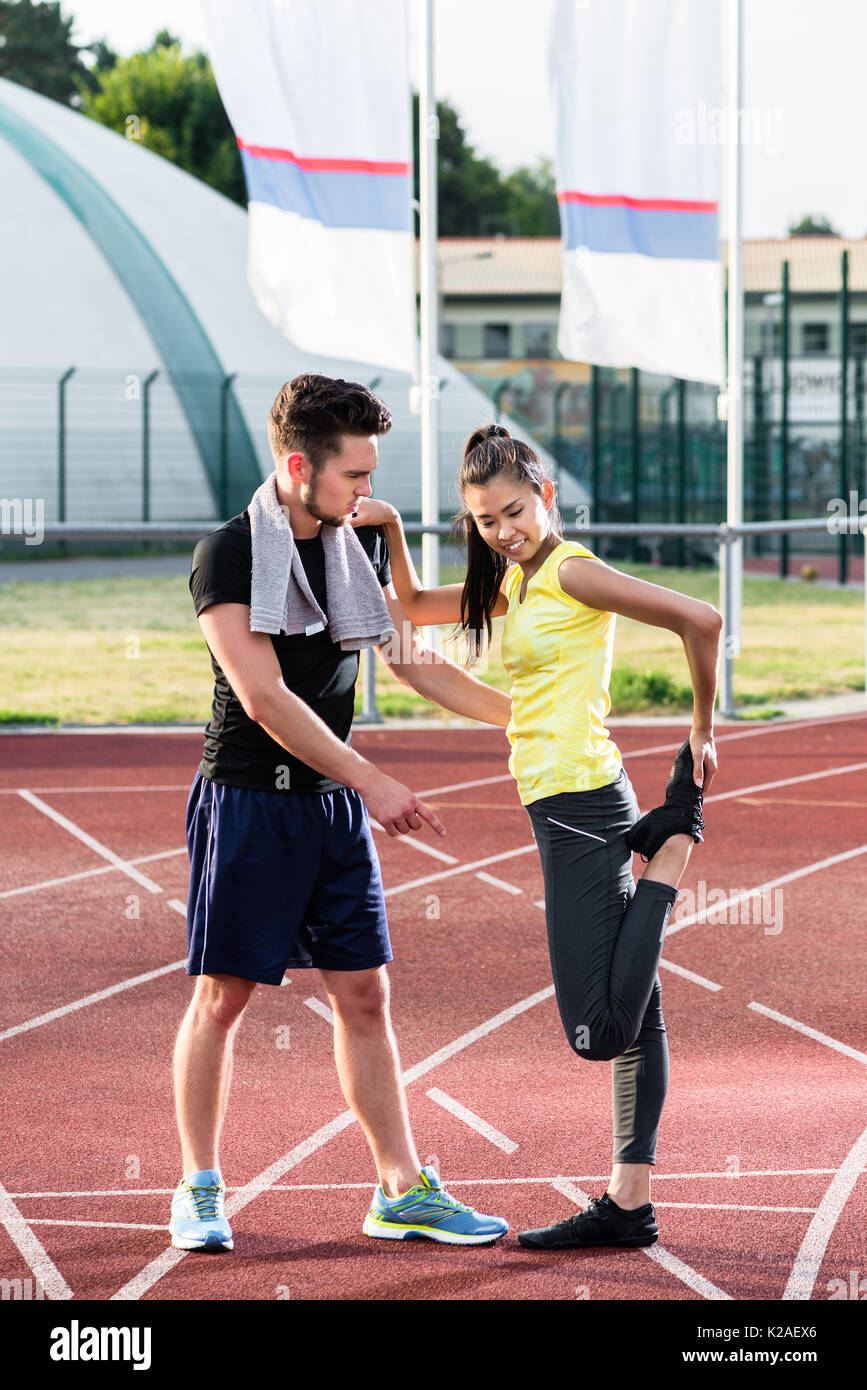 Man and woman on cinder track of sports arena stretching exercis Stock Photo