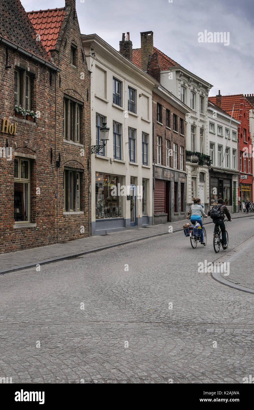 A couple cycle down a quiet cobbled street in the medieval city of Brugge / Bruges in West Flanders, Belgium Stock Photo
