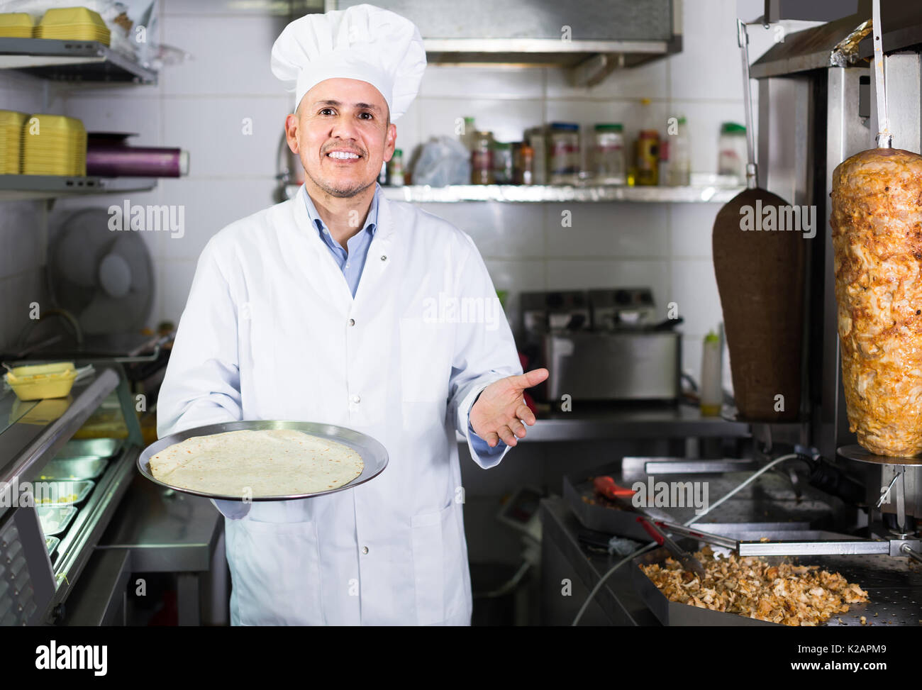 Happy Spanish Mature Man Cook Making Kebab Dish On Kitchen In Fast