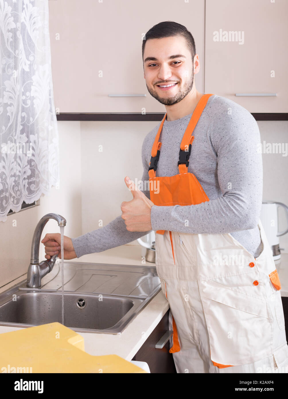 Smiling plumber in uniform successfully working at home of client Stock Photo