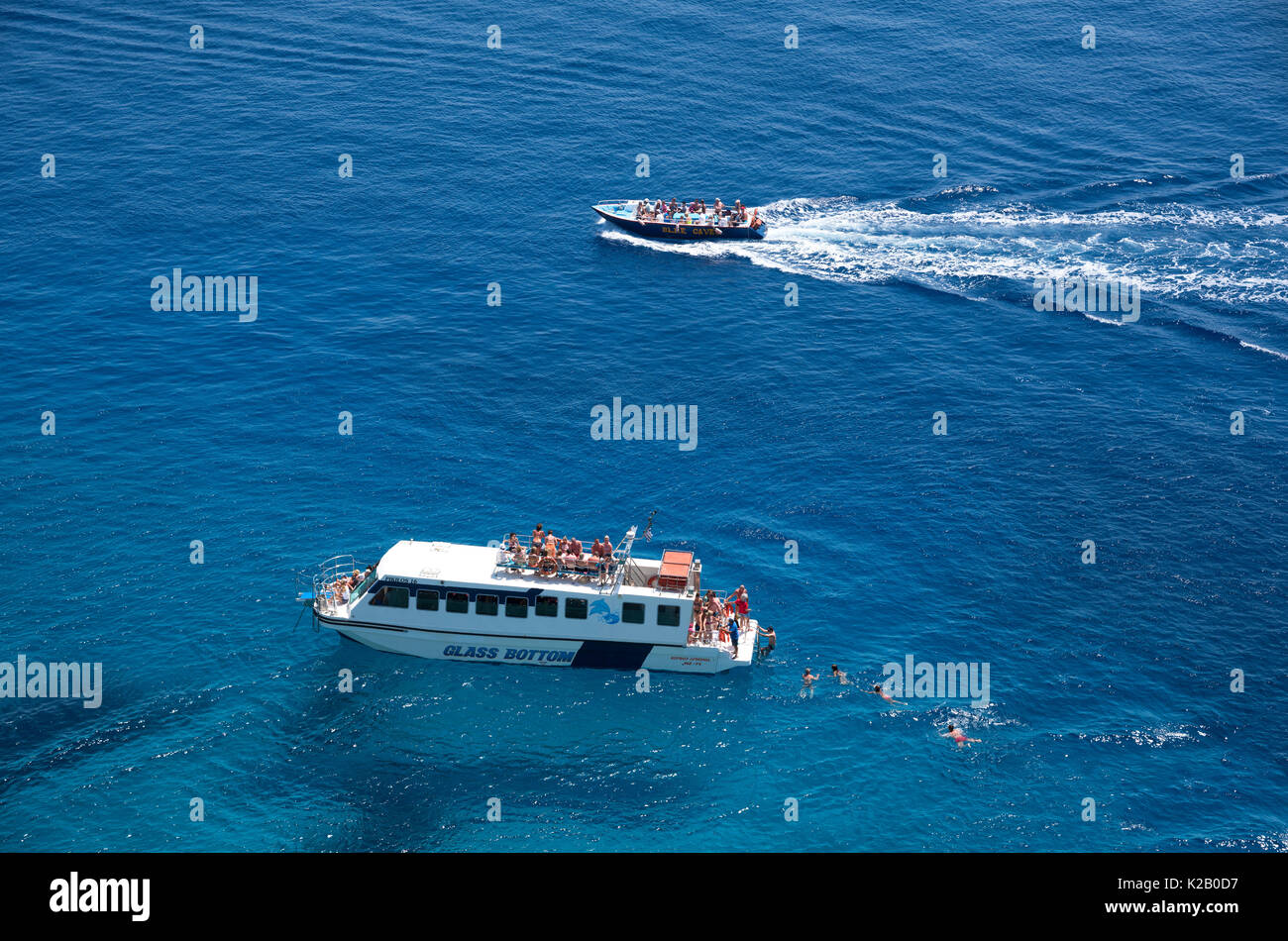 Glass bottom boat with tourists swimming around it, on an escursion to the Blue Caves, on the Greek island of Zakynthos Stock Photo