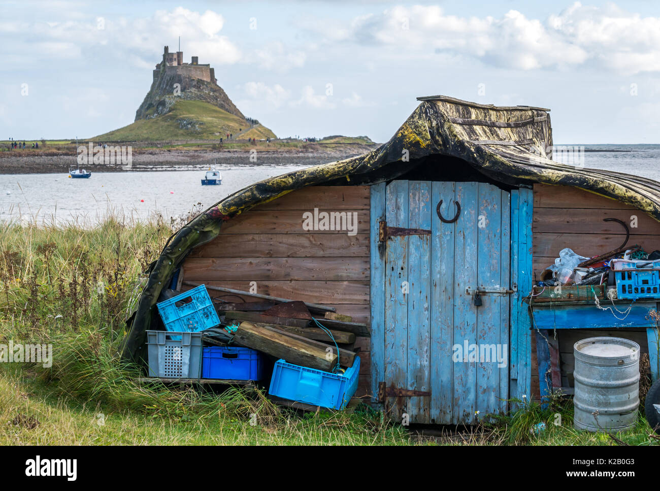 Close up of upturned boats on Holy Island, Lindisfarne, former herring fleet vessels, now converted into sheds, with castle in background Stock Photo