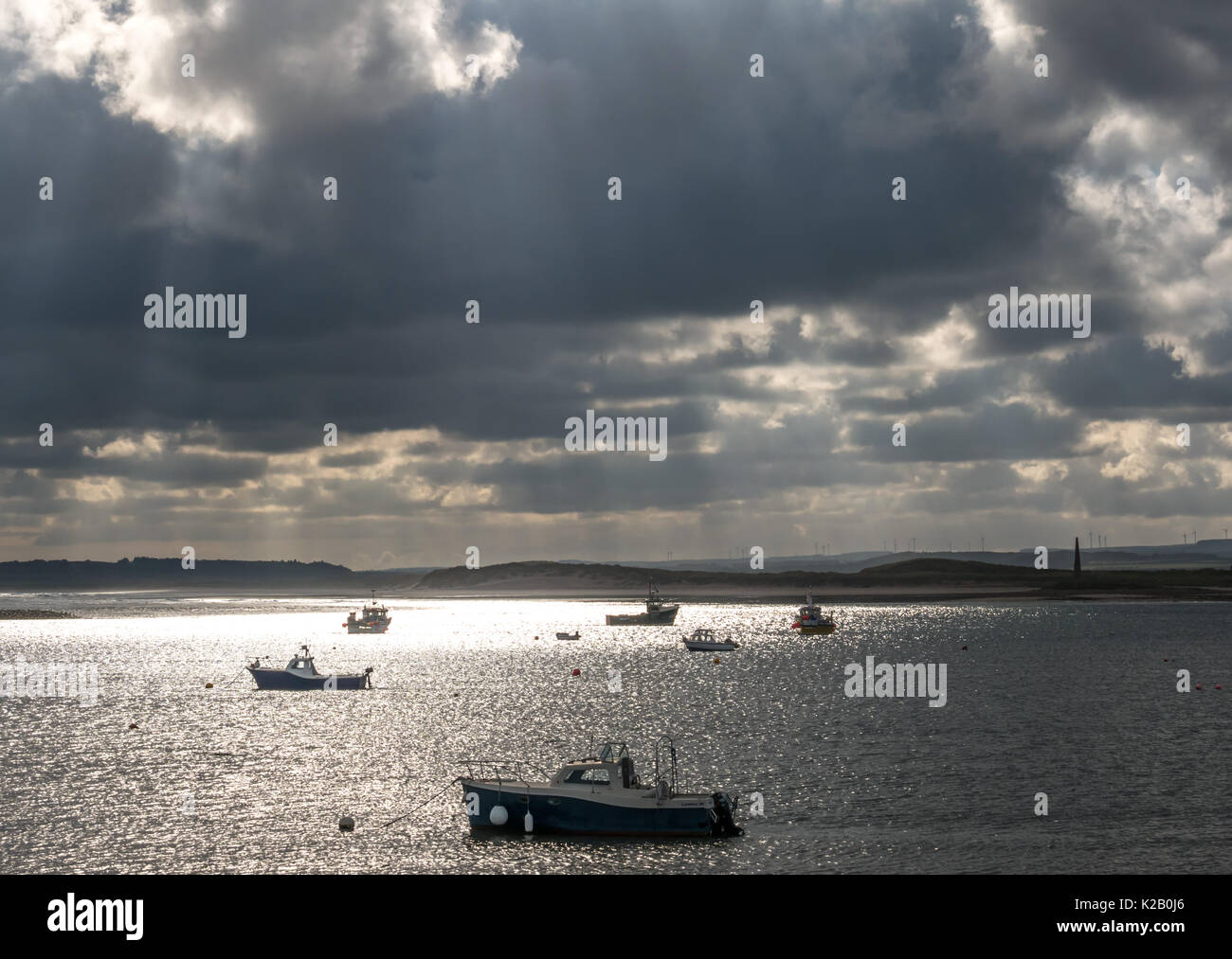 View from Holy Island, Lindisfarne to Northumberland coast with moored boats in Hen Pool and dramatic sun rays streaming through clouds, England, UK Stock Photo