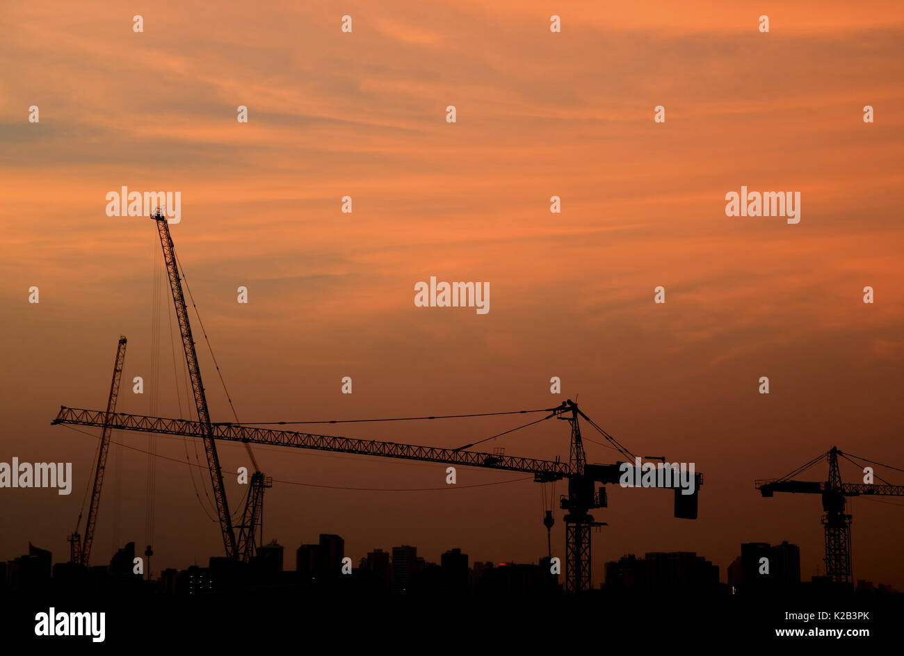 Silhouette of construction cranes against evening pastel orange sky Stock Photo
