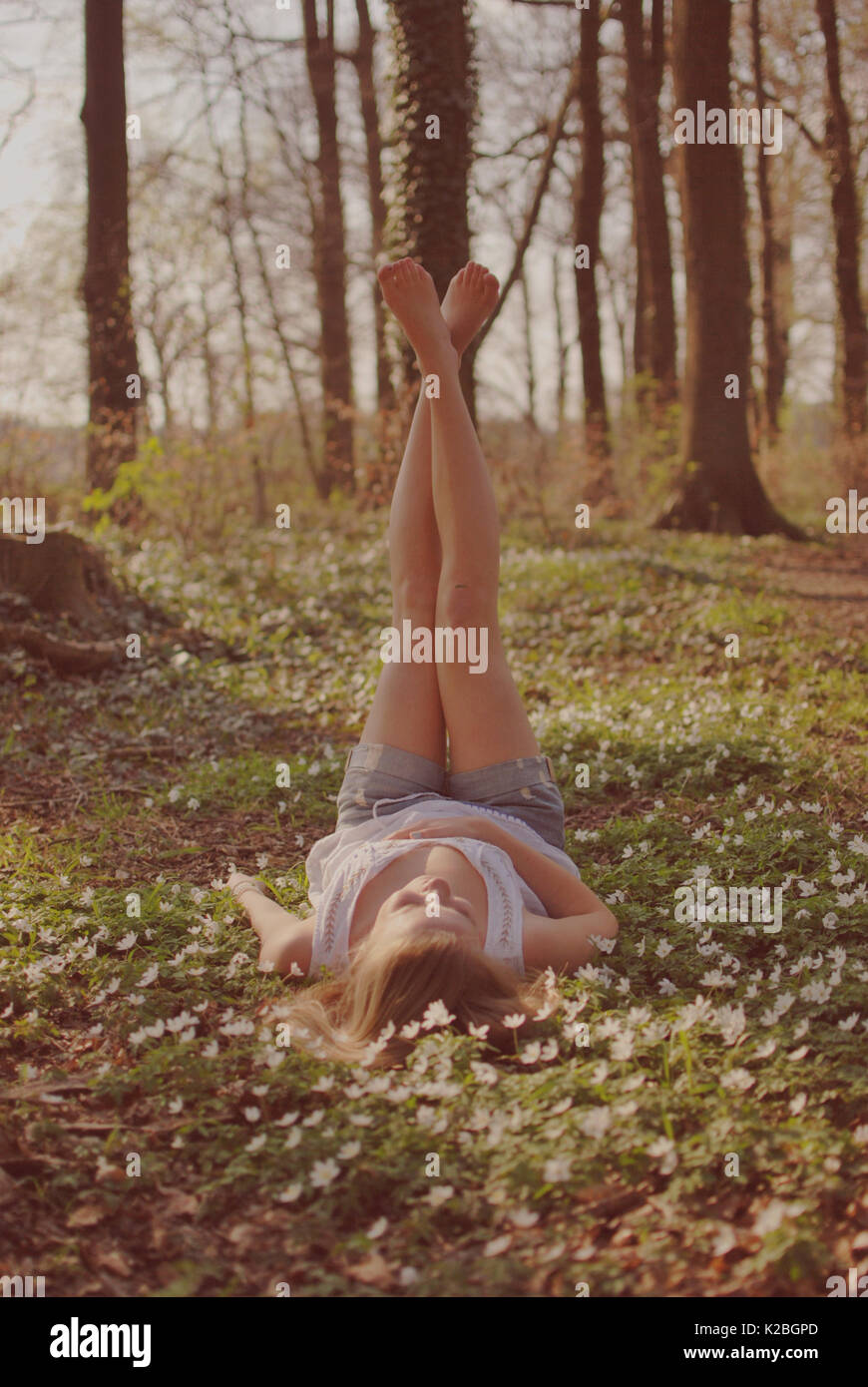 Girl lies on the forest floor and stretches her leg up Stock Photo