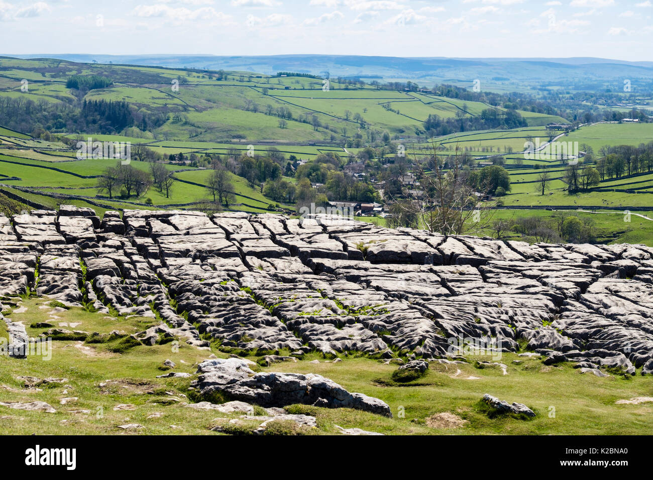 Clints and grikes in limestone pavement at top of Malham Cove with village beyond. Malham Yorkshire Dales National Park England UK Stock Photo