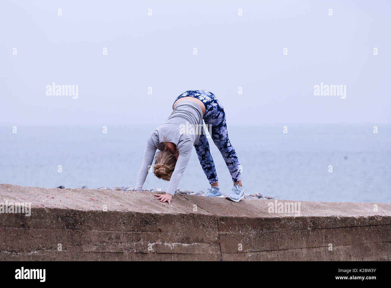 Young woman doing downward dog, a yoga move on the sea wall in Cromer, Norfolk, UK Stock Photo