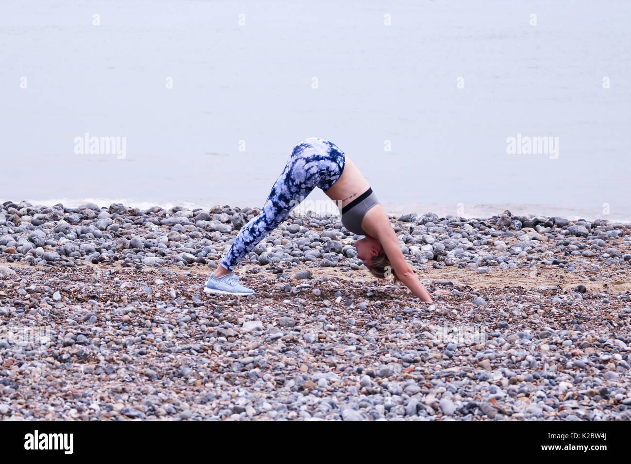 Young female going downward dog, a yoga position, on the beach in Cromer, Norfolk, UK. Stock Photo