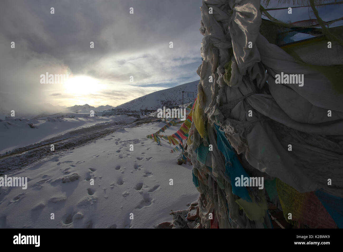Tattered prayer flags in snow covered landscape with grey clouds, Baima Snow Mountain Nature Reserve, Yunnan Province, China. April 2010. Stock Photo