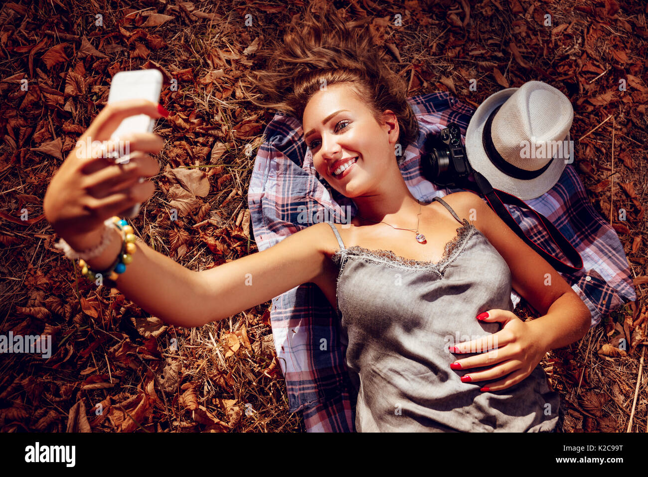 Beautiful smiling girl taking selfie in nature in autumn. She is lying on the falls leaves Stock