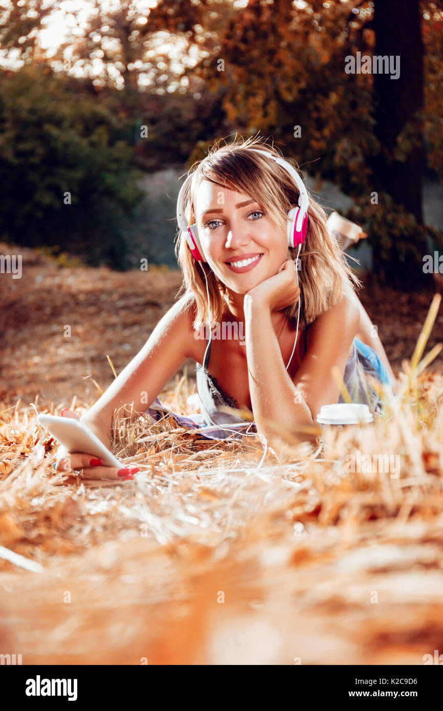 Cute smiling young woman lying on the withered grasses and listening music. Looking at camera. Stock Photo