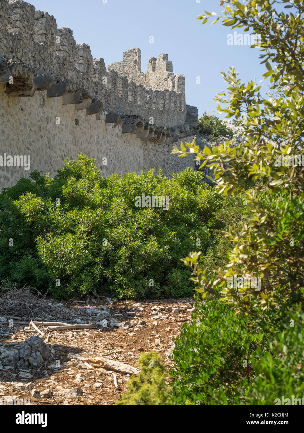 a view of an ancient stone wall ruins with battlements and ramparts surrounded by woods forest trees Croatian coastline clear blue sky Stock Photo