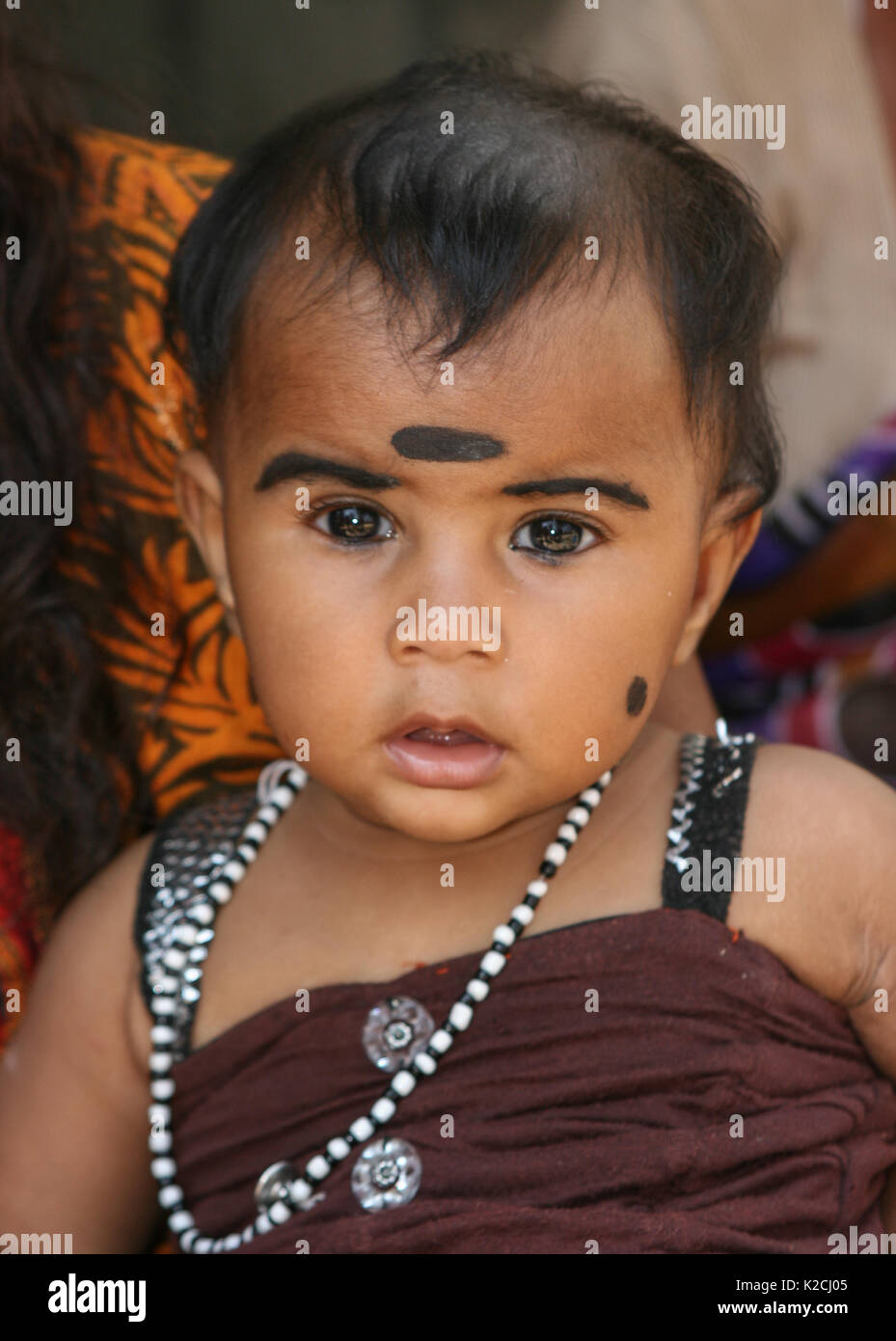 head and shoulder of a female Asian Indian young baby toddler girl made up with black kohl eyeliner pencil cosmetics looking at into camera Stock Photo