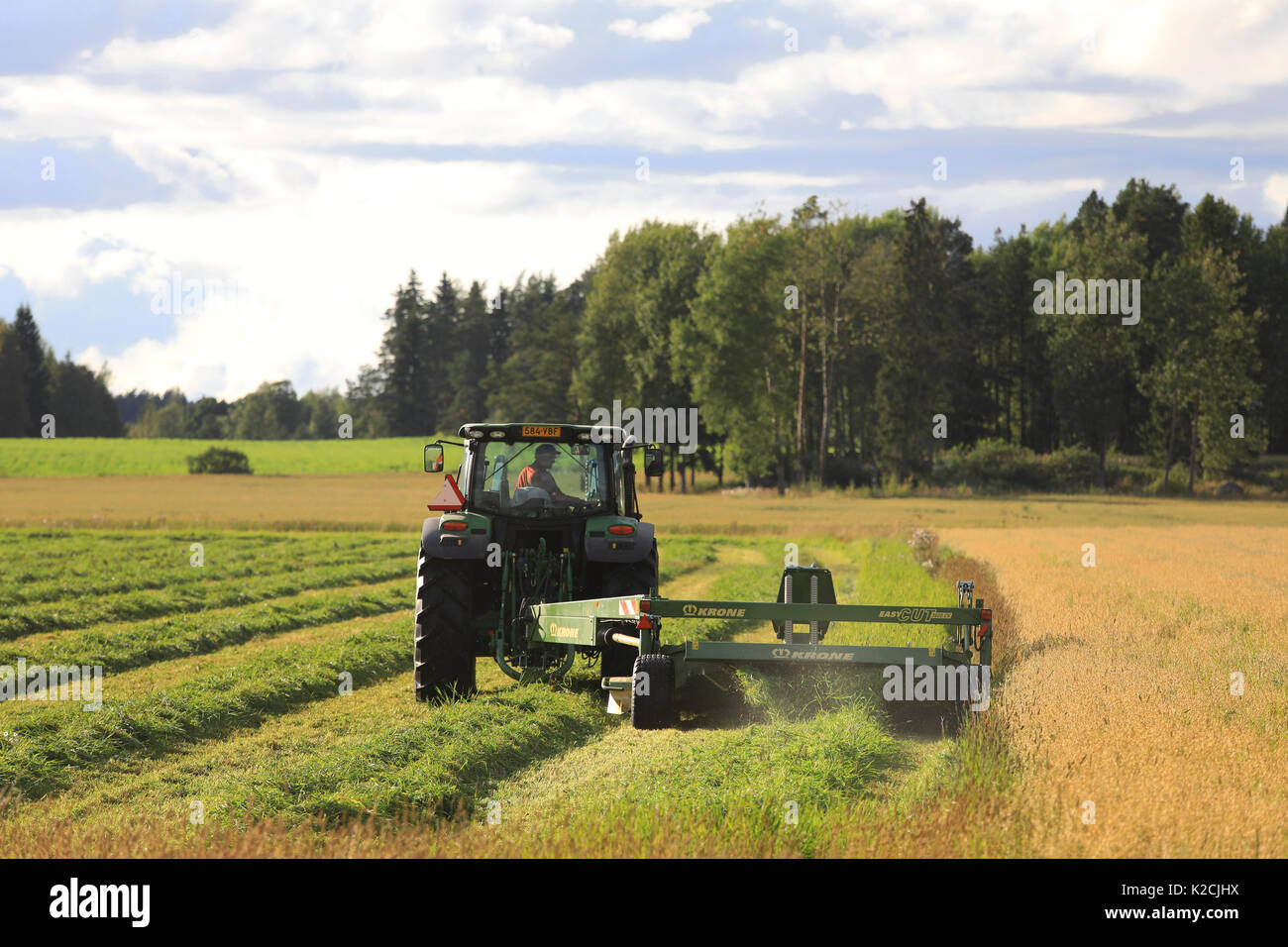 JOKIOINEN, FINLAND - AUGUST 25, 2017: Farmer cuts hay with Krone EasyCut 3600 CV mower pulled by John Deere tractor on late summer evening. Stock Photo