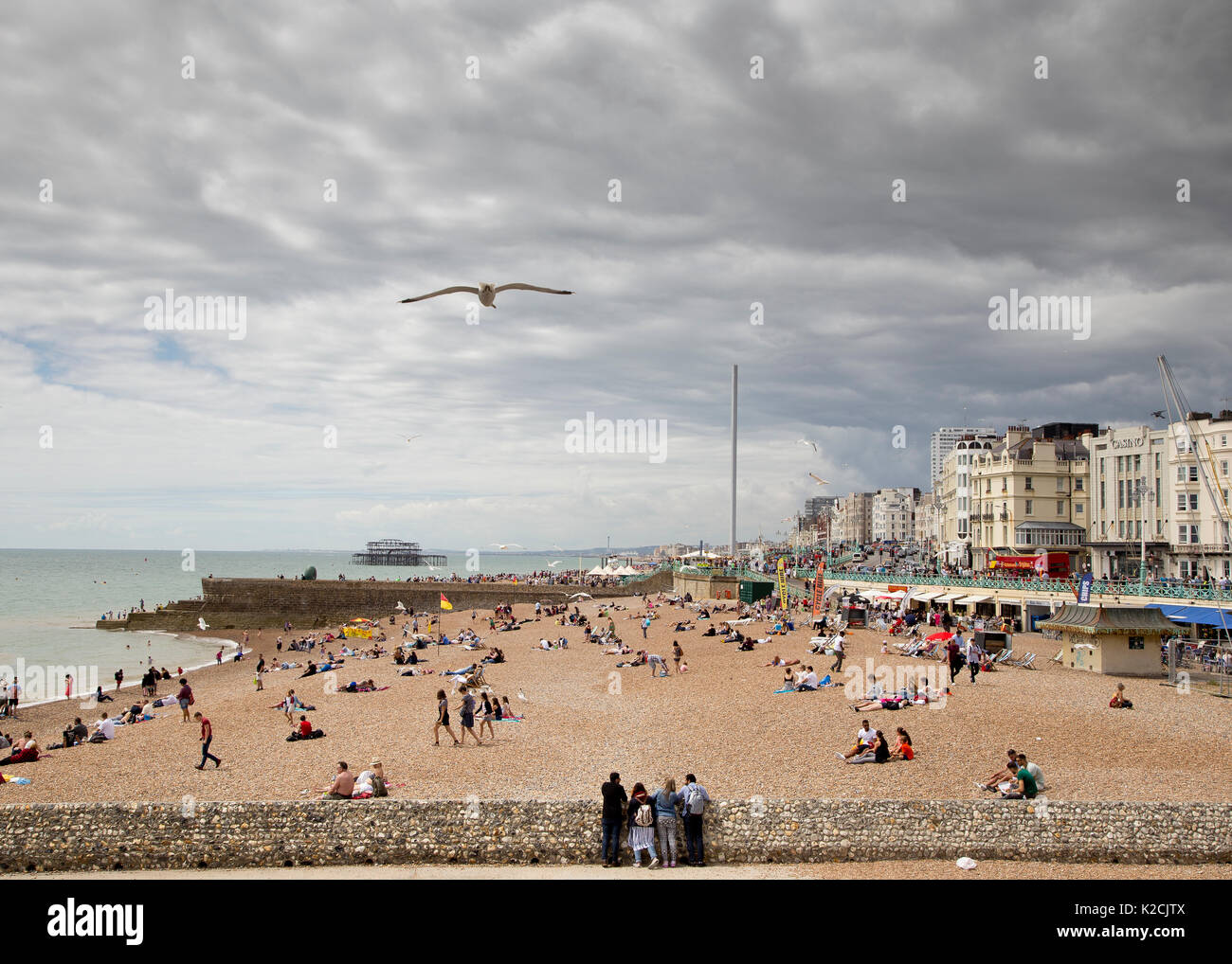 Landscape view of Brighton beach on an overcast but hot day with many people enjoying the beachfront Stock Photo