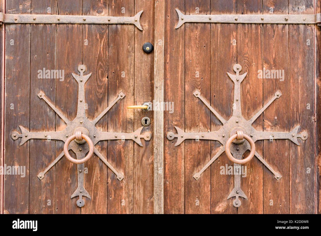 Old wooden doors with ornamentals from the 19th century. Wrought ironworks decorate the two doors. Modern lock and handle on one door. Stock Photo