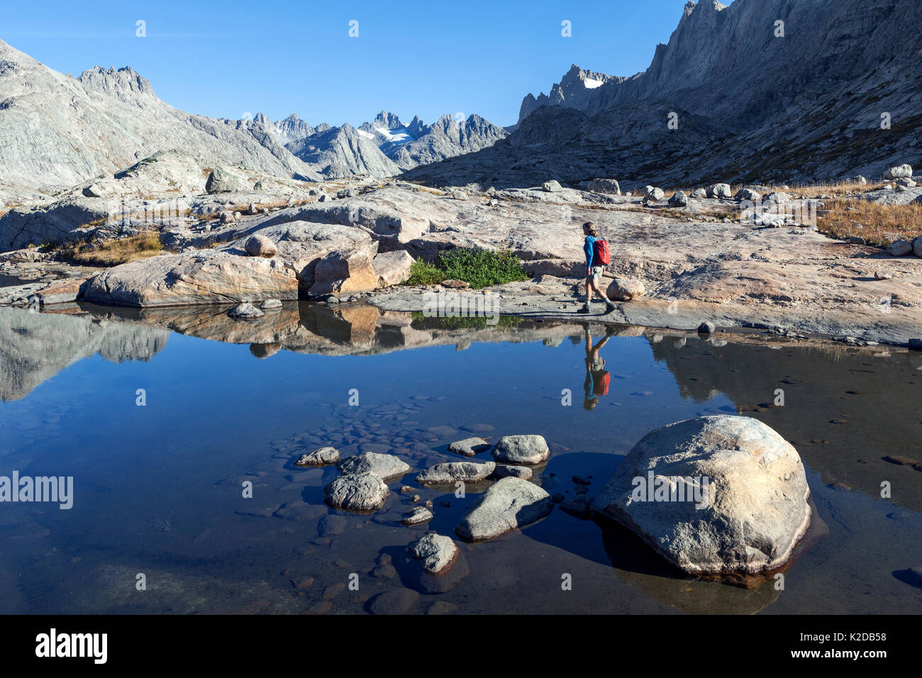 Woman hiker walking round mountain lake in Titcomb Basin in Wind River Range of Bridger Wilderness, Bridger National Forest, Wyoming, USA. September 2015. Model released Stock Photo