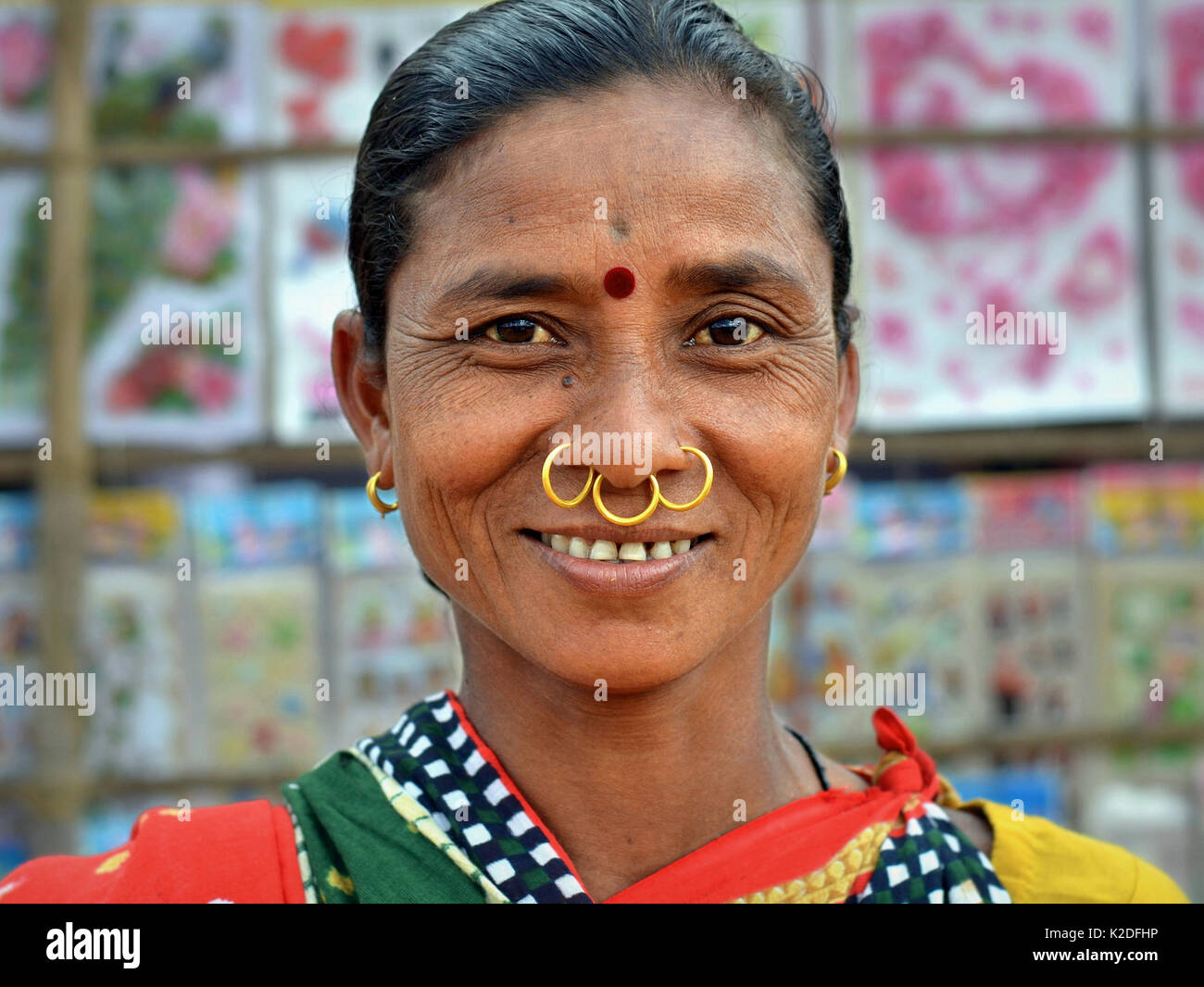 Indian Adivasi woman (Dongria Kondh tribe) with three golden nose rings, tribal earrings and red bindi on her forehead smiles for the camera. Stock Photo