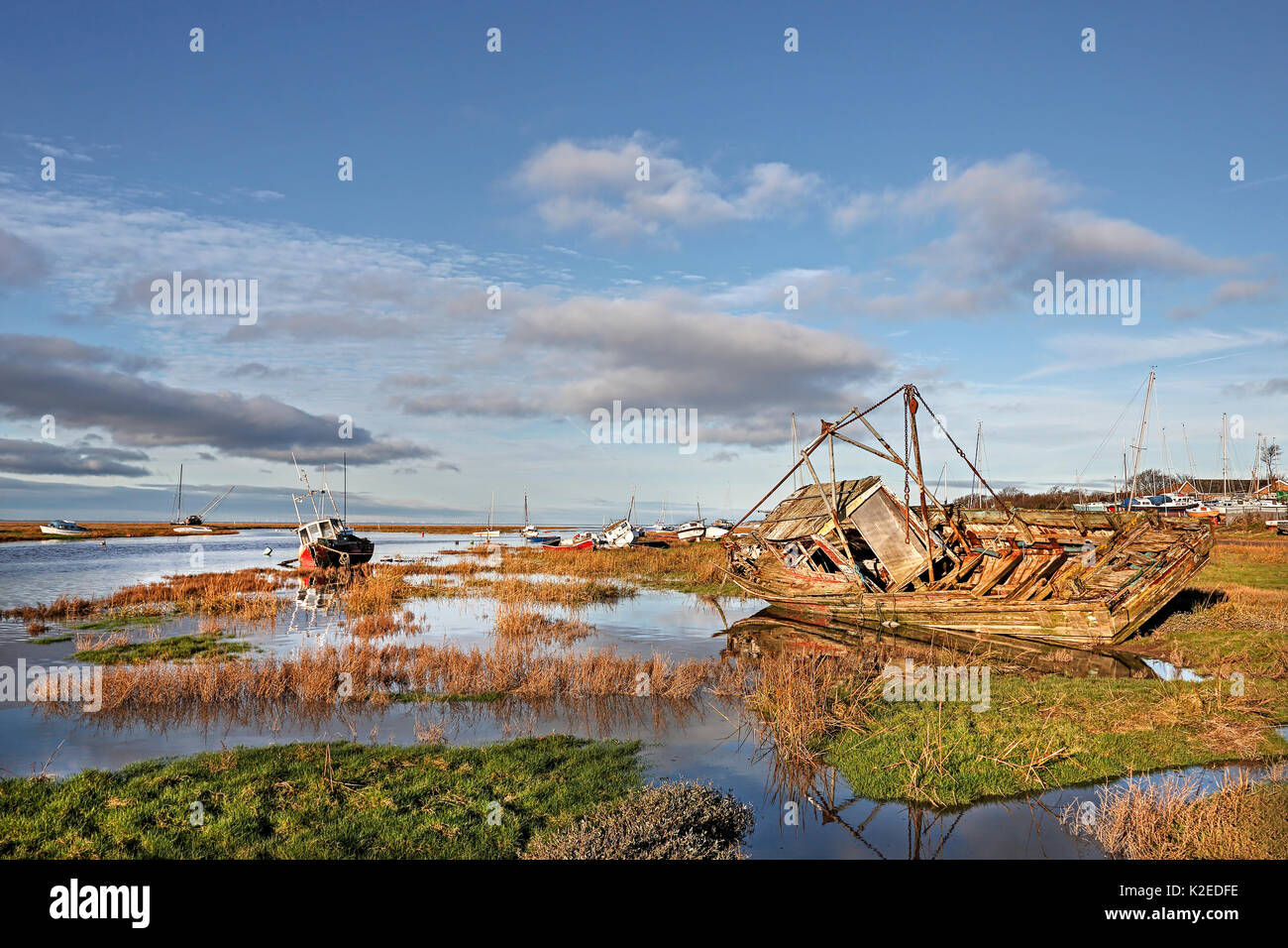Old boats alongside channel with rising tide in Dee Estuary in early morning sunlight. Heswall, Wirral, Merseyside, UK January. Stock Photo