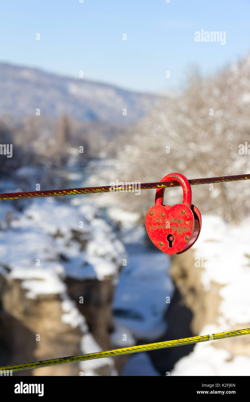 old closed red padlock in heart shape on a background of a winter ...