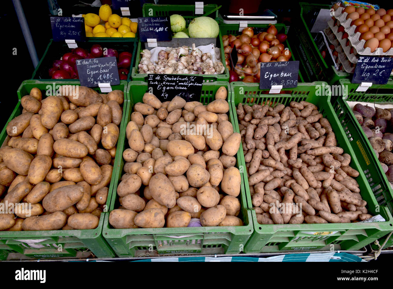 Market stall offering different sorts of potatos, garlic and onions Stock Photo