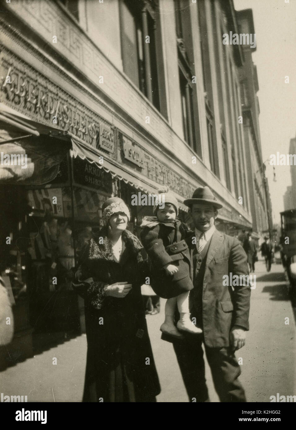 Antique c1920 photograph, family poses on the sidewalk in front of a clothing store, possibly called Hetherington Haberdashers. Signage is visible for Arrow Shirts and Soda. LOCATION UNKNOWN, possibly New York City. SOURCE: ORIGINAL PHOTOGRAPH. Stock Photo