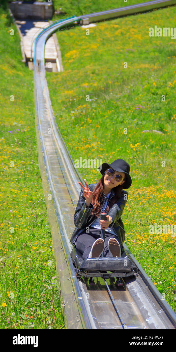 Asian woman riding summer toboggan (sled) down a hill through the