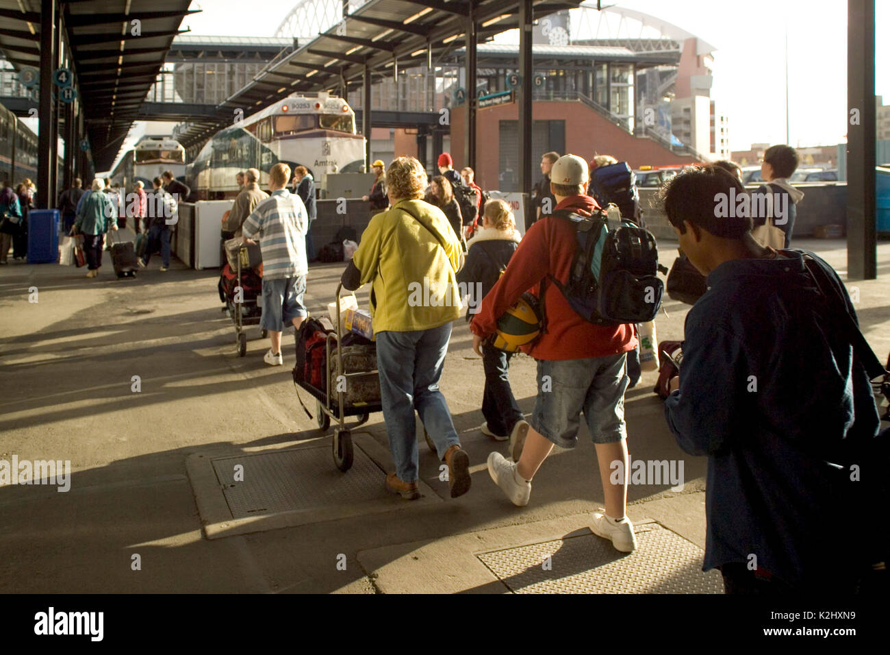In bright afternoon sunlight, departing passengers with carry on