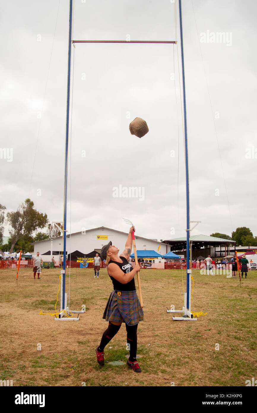 A kilted young woman competes in the 'Sheaf Toss' at a Scottish festival in Costa Mesa, CA, using a pitchfork to toss a 16-pound burlap bag of straw over a bar. Stock Photo