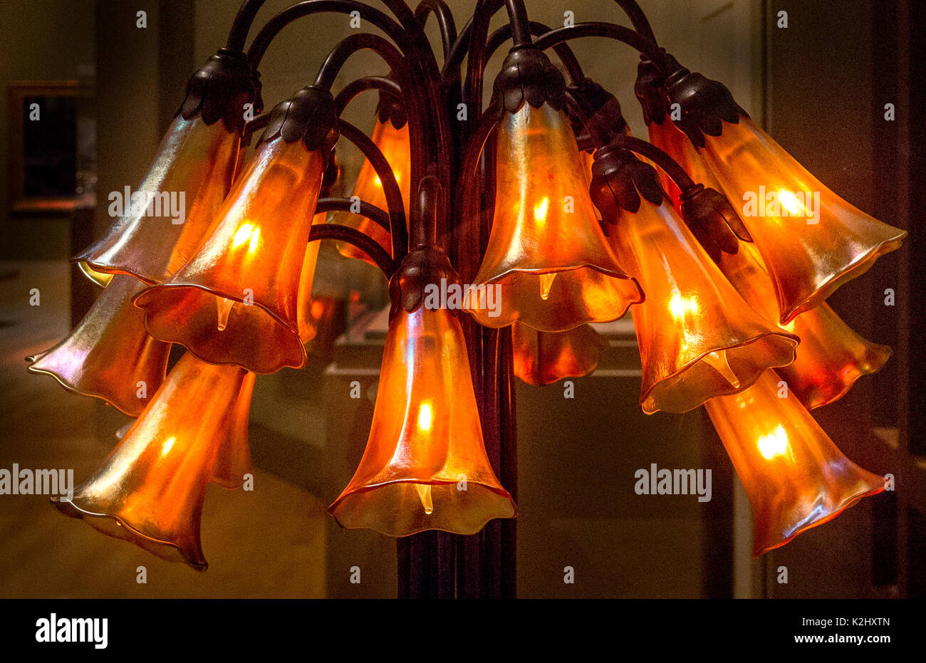 Twelve drop cluster Lilly blossoms in orange-colored blown glass decorate a Tiffany Studios bronze lamp from 1902. Stock Photo