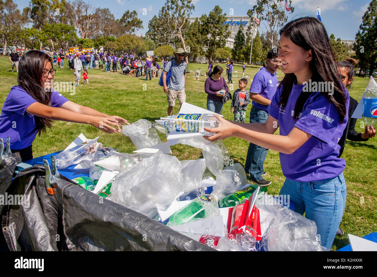 Wearing purple uniform T shirts, two Asian American young adult instructors collect expended water rockets at an outdoor rocket launching festival in Huntington Beach, CA. Made out of a plastic soda bottle, a water rocket uses water as its reaction mass. The water is forced out by compressed air. It operates on the principle of Newton's third law of motion Stock Photo